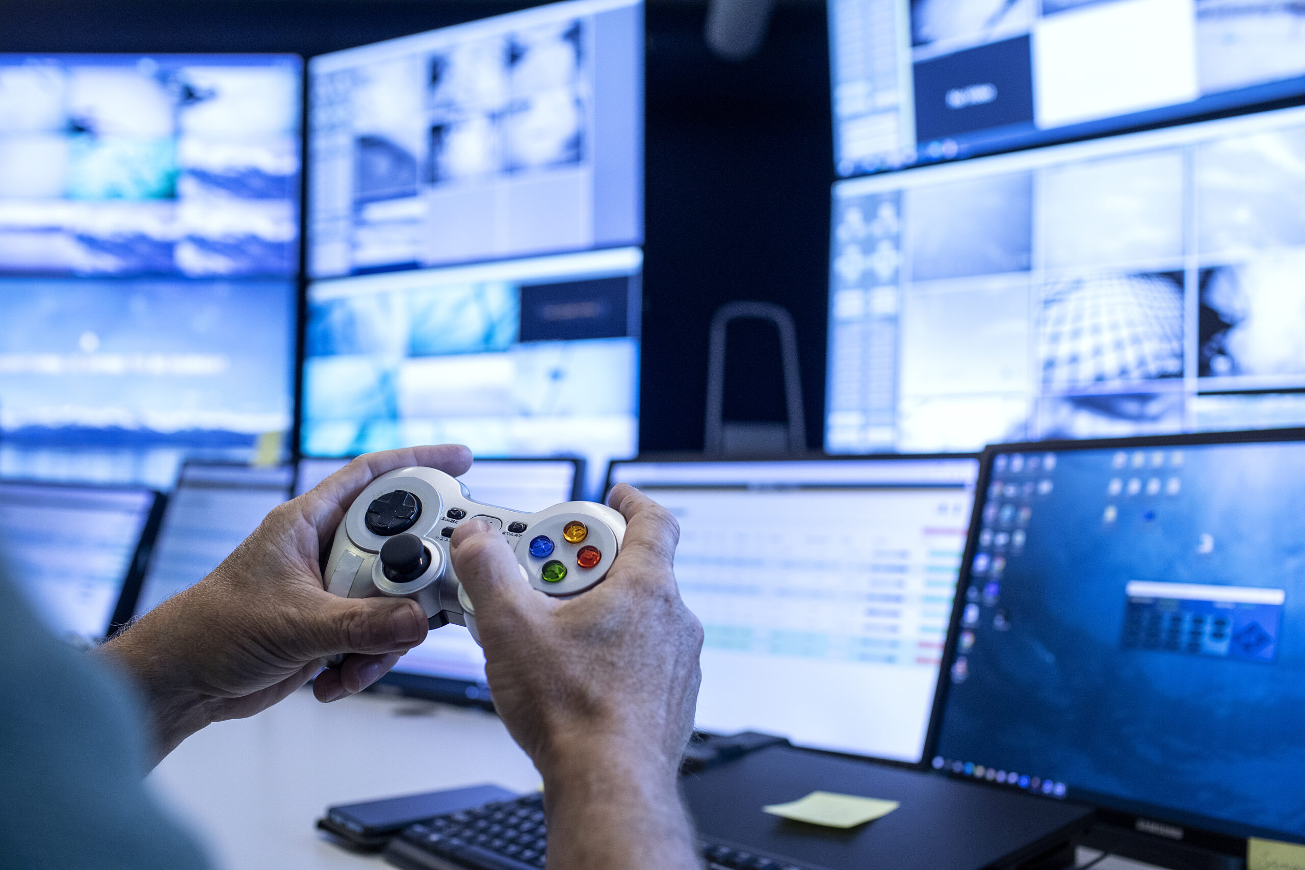 Image of person holding console controller in front of many PC screens taken at Lingalaks' viewing center